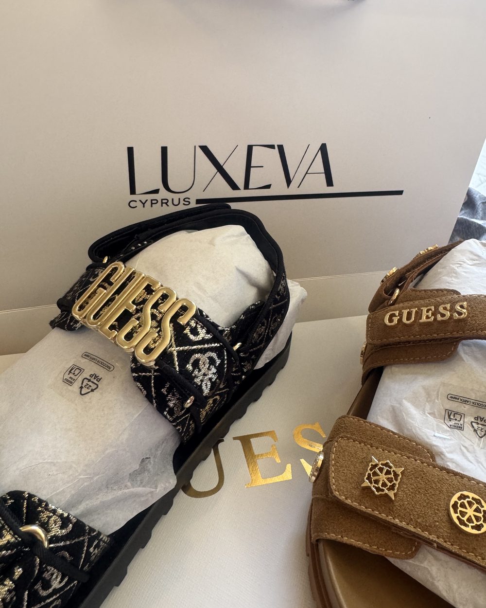 Guess logolu iki çift sandalet, Luxeva Cyprus kutusunun üstünde